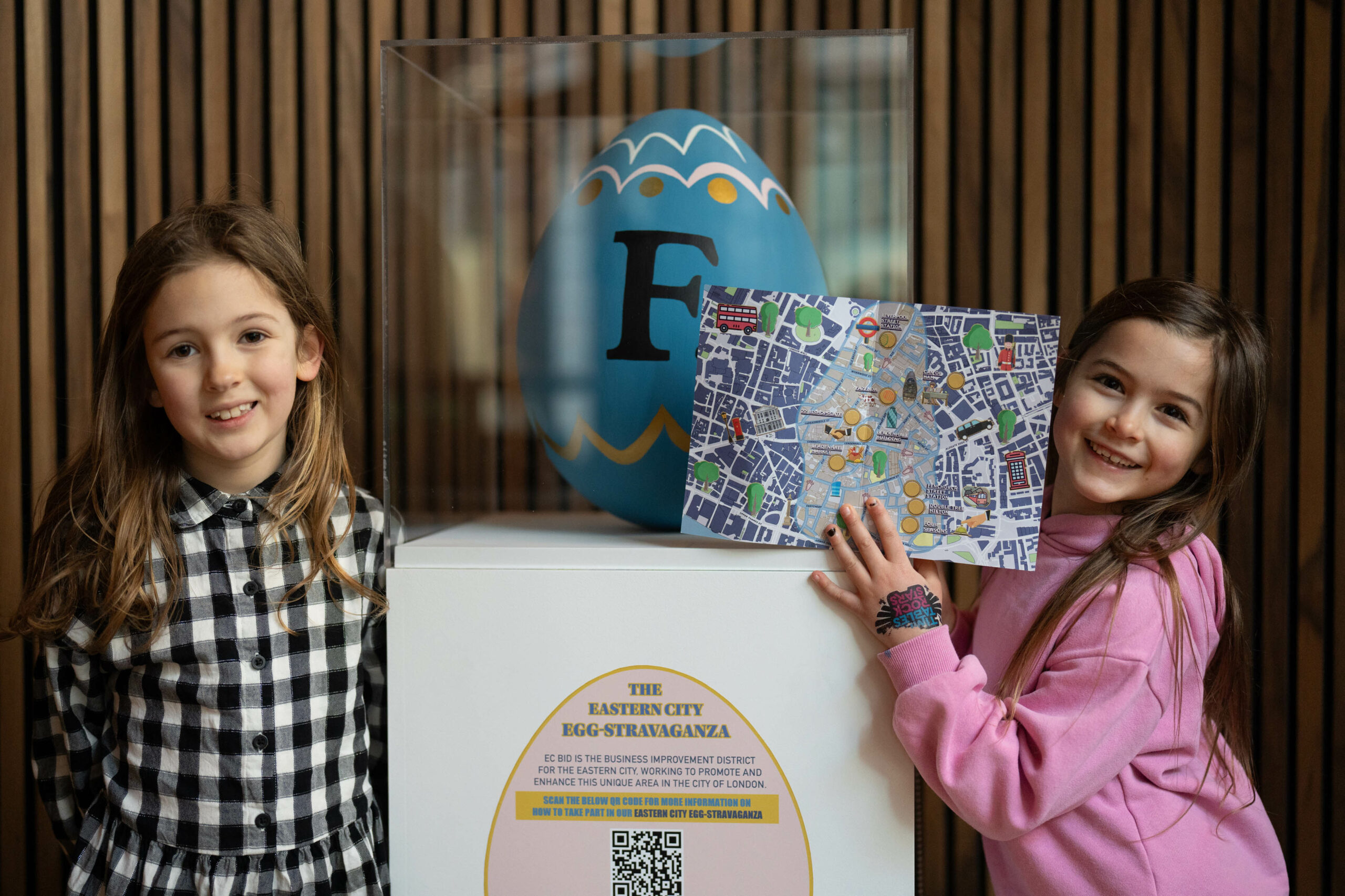 Two girls smile and post with a blue Easter Egg at Fazenda, as part of the Easter trail for EC BID